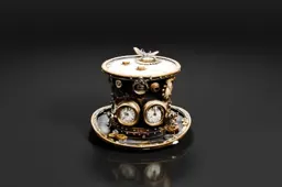 Small, ornate clock with a round, cylindrical body and a lid
